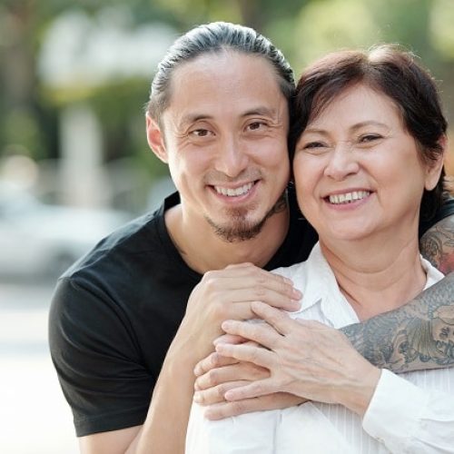 Portrait of happy Asian family embracing each other and smiling at camera while walking outdoors